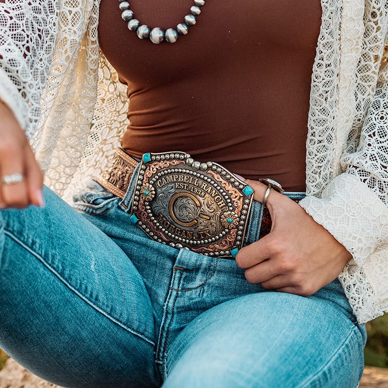 Woman wearing a personalized western belt buckle with a ranch brand and turquoise stones